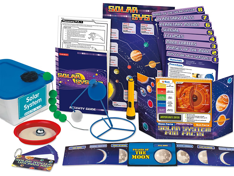 Solar system educational kit with books, charts, models, and moon phases wheel on a white surface.