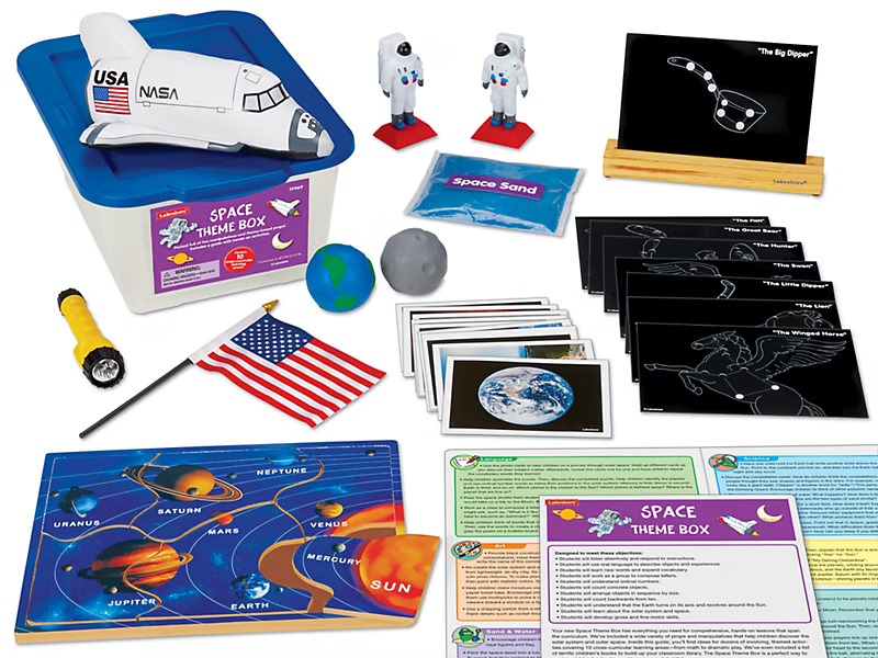 Space-themed educational kit with a labeled box, miniature space shuttle, astronaut figures, constellation cards, planets, flag, and flashlight. 
